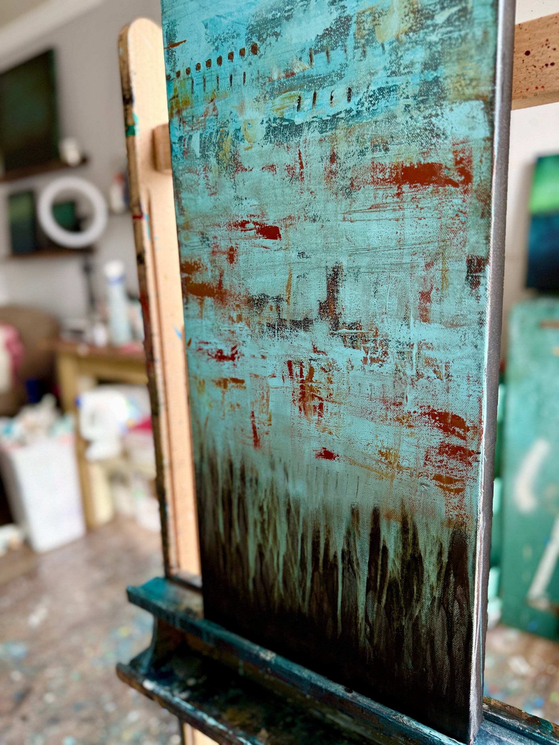 Fading Recollections, 12x36" abstract painting by Michelle Ramos shown on an easel in the studio. Turquoise, rust, and ochre tones with rich layered texture.