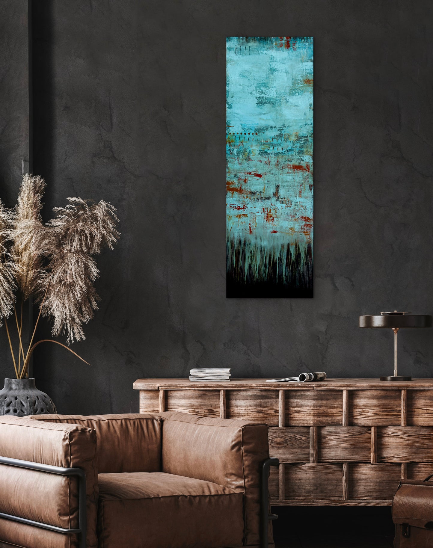 Fading Recollections, 12x36" vertical abstract painting by Michelle Ramos displayed in a modern dark interior above a brown leather sofa. Moody turquoise and rust artwork with atmospheric texture.