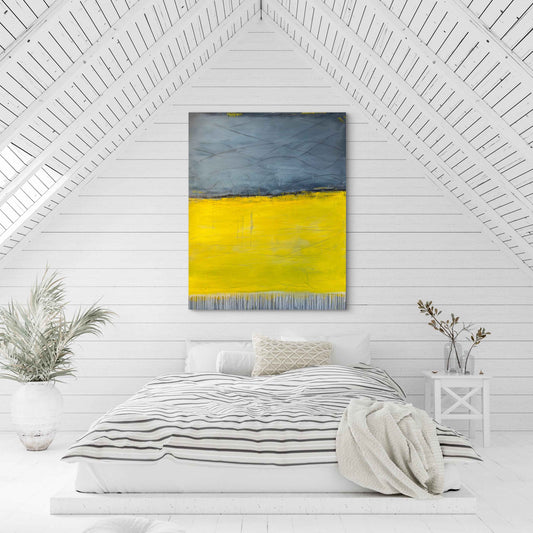 It Melts Into Wonder, a large abstract painting with blue-gray upper tones and a vibrant yellow lower section, displayed above a bed in a bright, neutral bedroom.