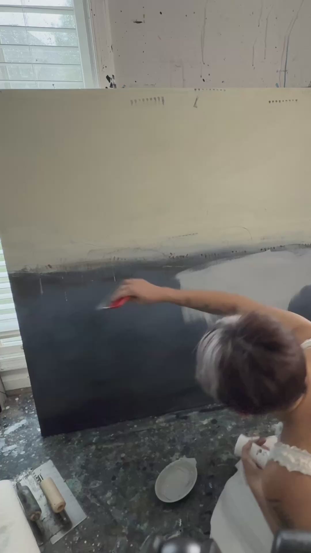 Artist painting a large abstract canvas in muted neutral tones, showing brushwork and layering during the creation process.